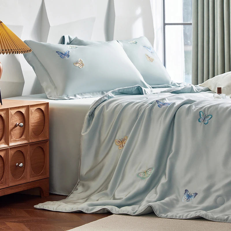 Bed with light blue bedding featuring butterfly designs, wooden nightstand, and lamp.