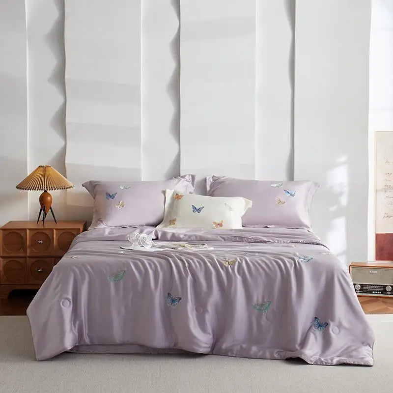 Bed with purple bedding featuring butterfly patterns, nightstand with lamp, and white walls.