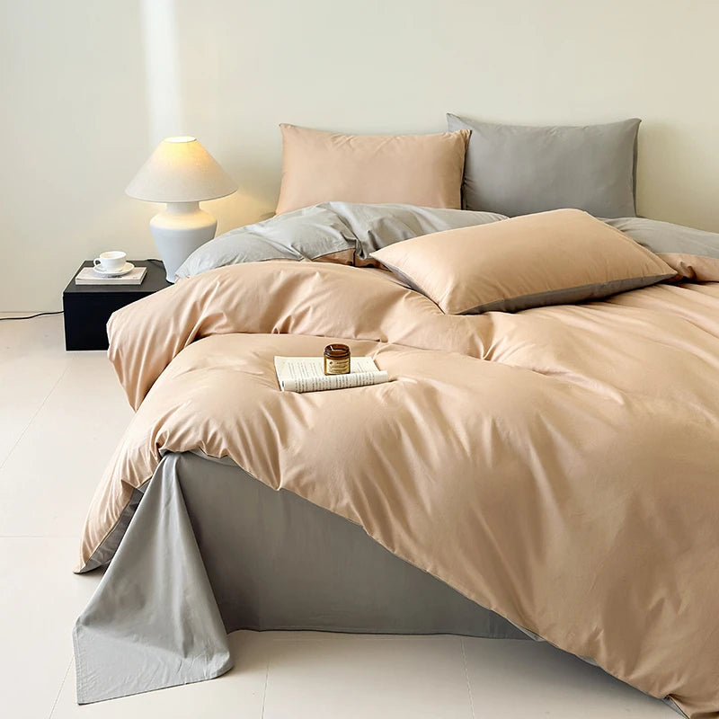 Beige and gray bedding set on a bed with a lamp and small table in the background.