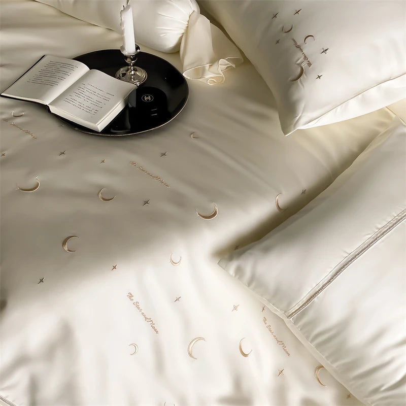 Beige bedding set with moon and star patterns, book, and candle on a table.
