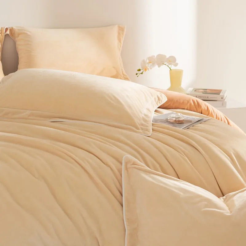 Beige comforter set on a bed with pillows and a small table in the background.