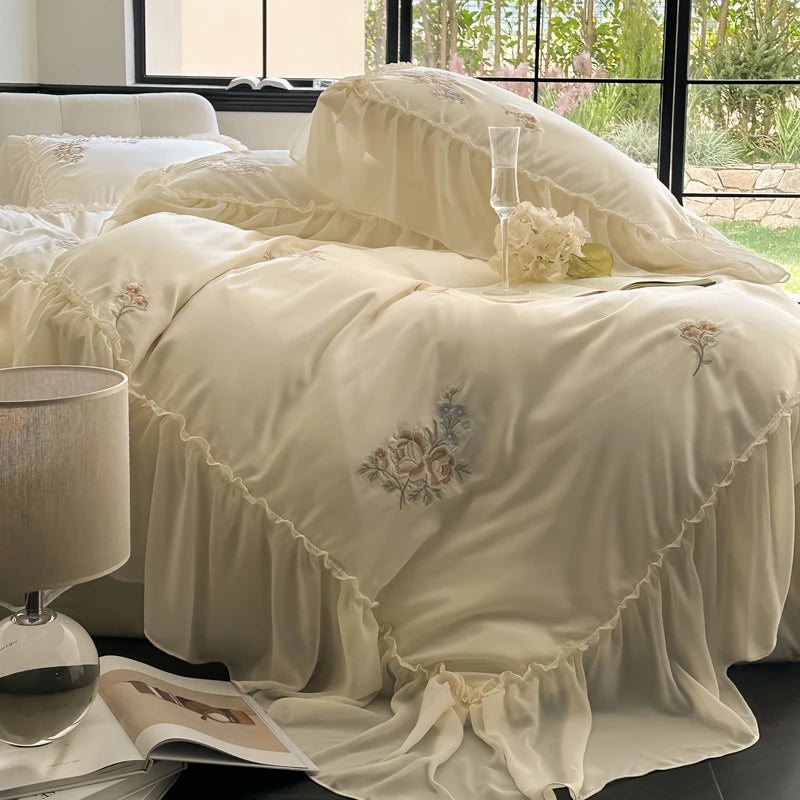 Beige embroidered bedding set on a bed with a lamp and magazine in the foreground.