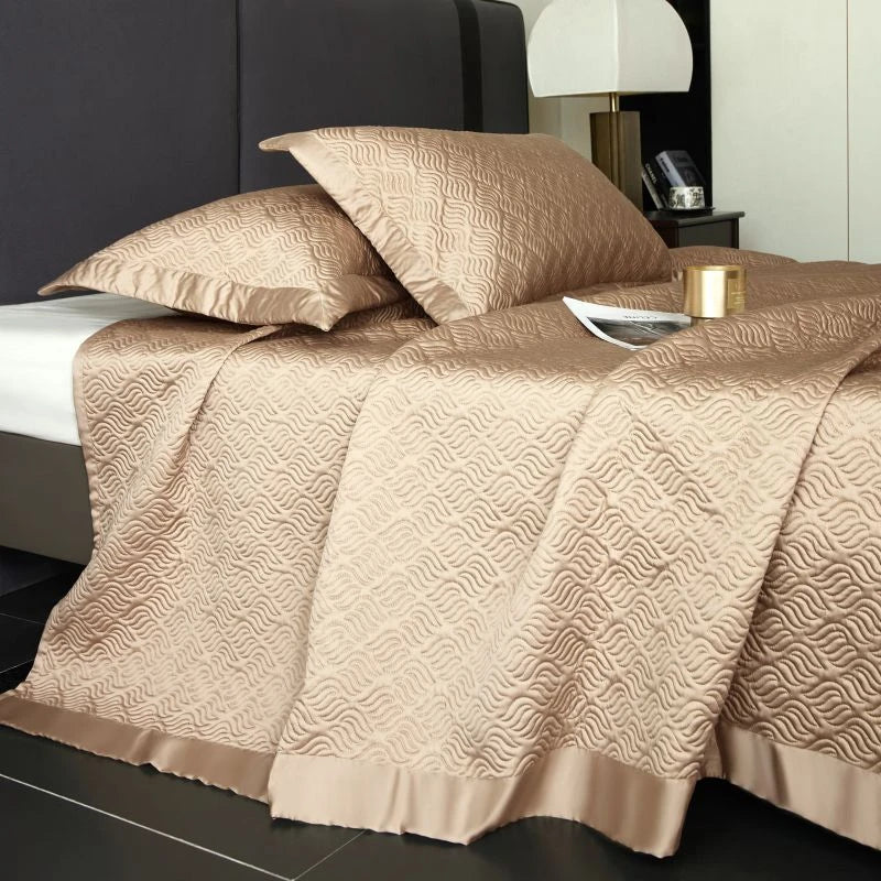 Beige patterned bedspread on a bed with pillows and a lamp in the background.