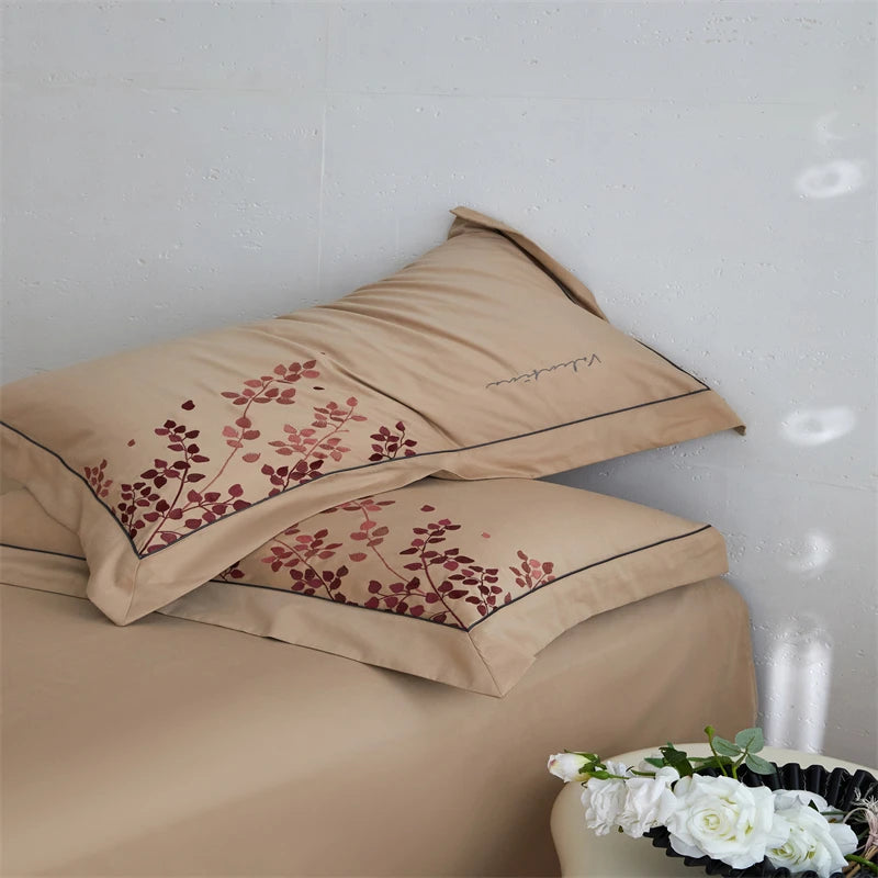 Beige pillowcases with floral embroidery on a bed against a light gray wall.
