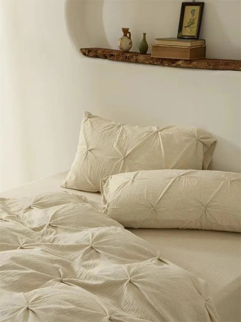 Beige pleated bedding set on a bed with a shelf in the background.