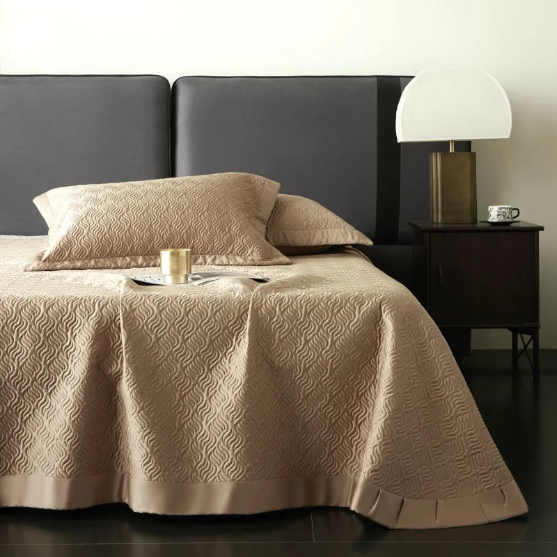 Beige quilted bedspread on a bed with a dark headboard and nightstand.