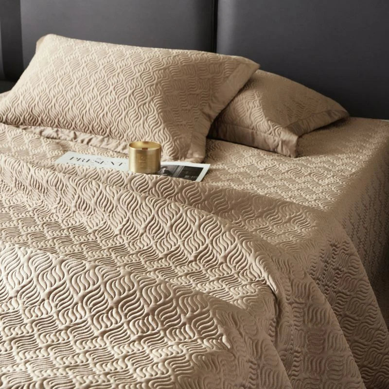 Beige textured bedspread on a bed with pillows and a candle.