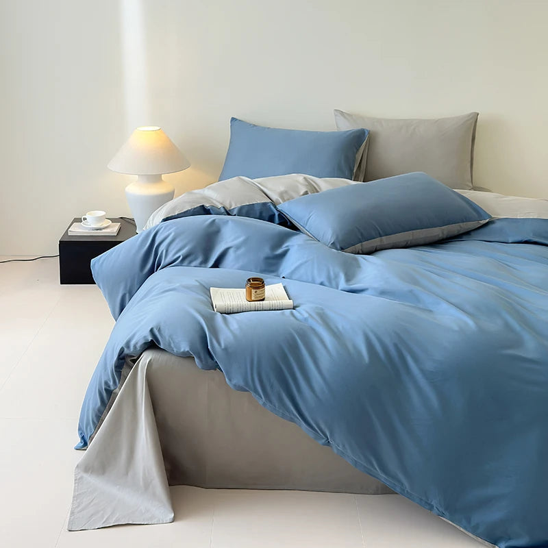 Blue bedding set on a bed in a bedroom with a lamp and small table.