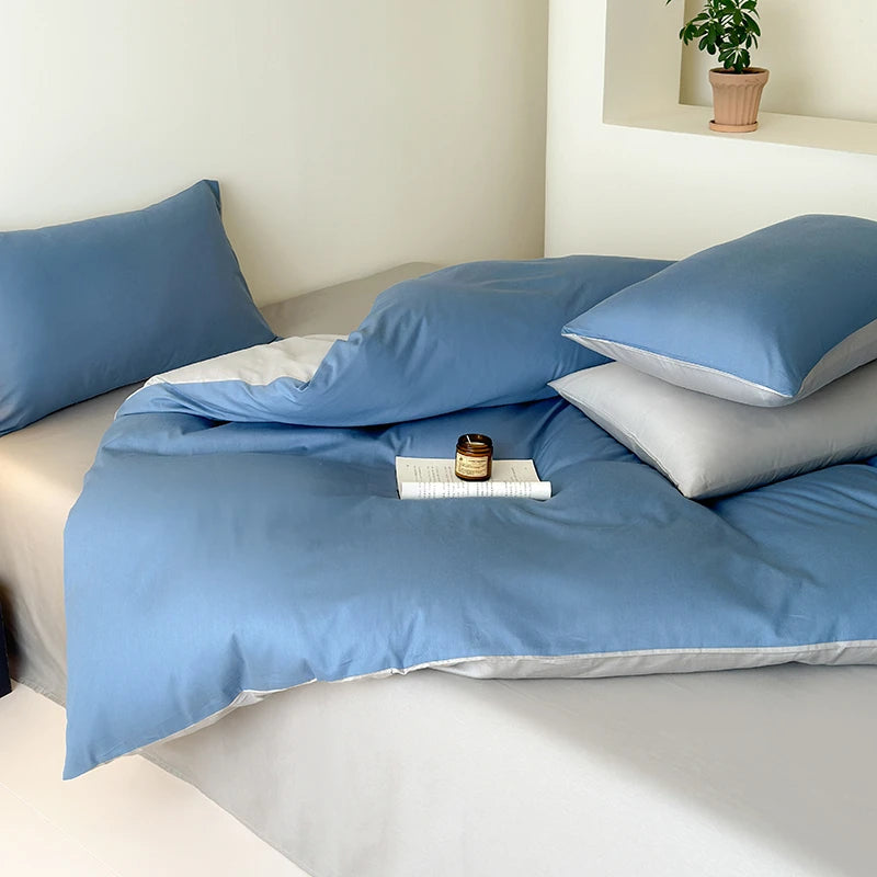 Blue bedding set on a bed with pillows and a small plant in the background.