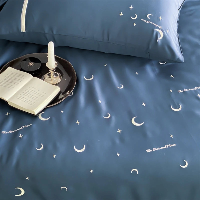 Blue bedding set with moon and star patterns, book, and candle on a tray.