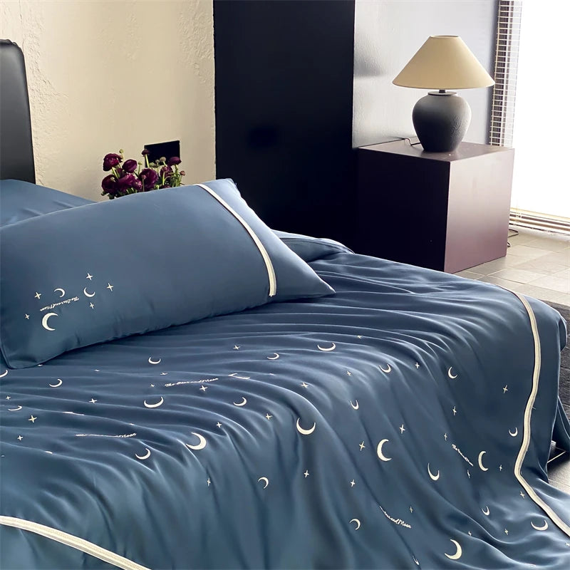 Blue bedspread with moon and star patterns on a bed in a bedroom setting.