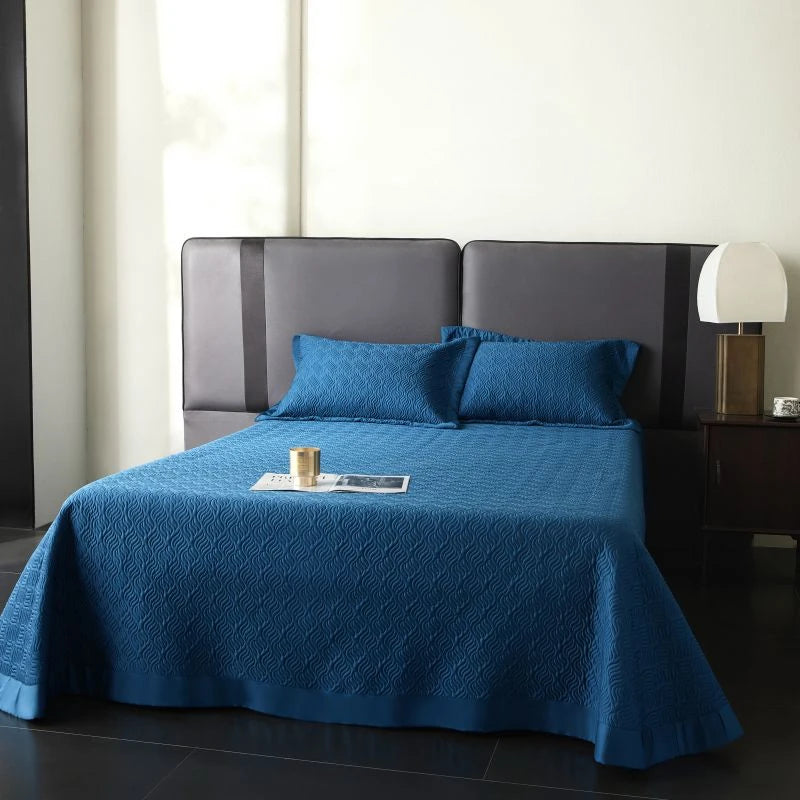 Blue quilted bedspread on a bed with pillows.