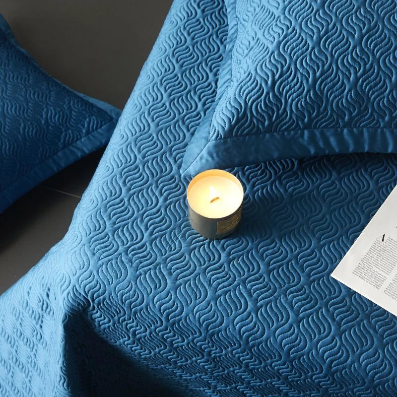Blue textured bed spread with a lit candle and paper on a dark surface