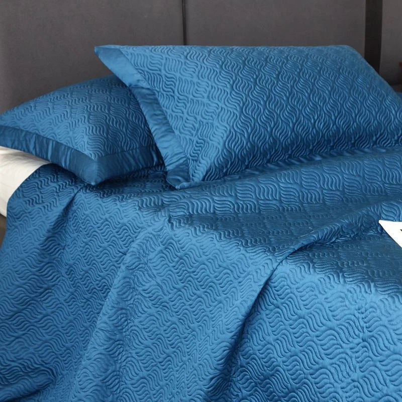 Blue textured bedspread on a bed with a gray wall in the background