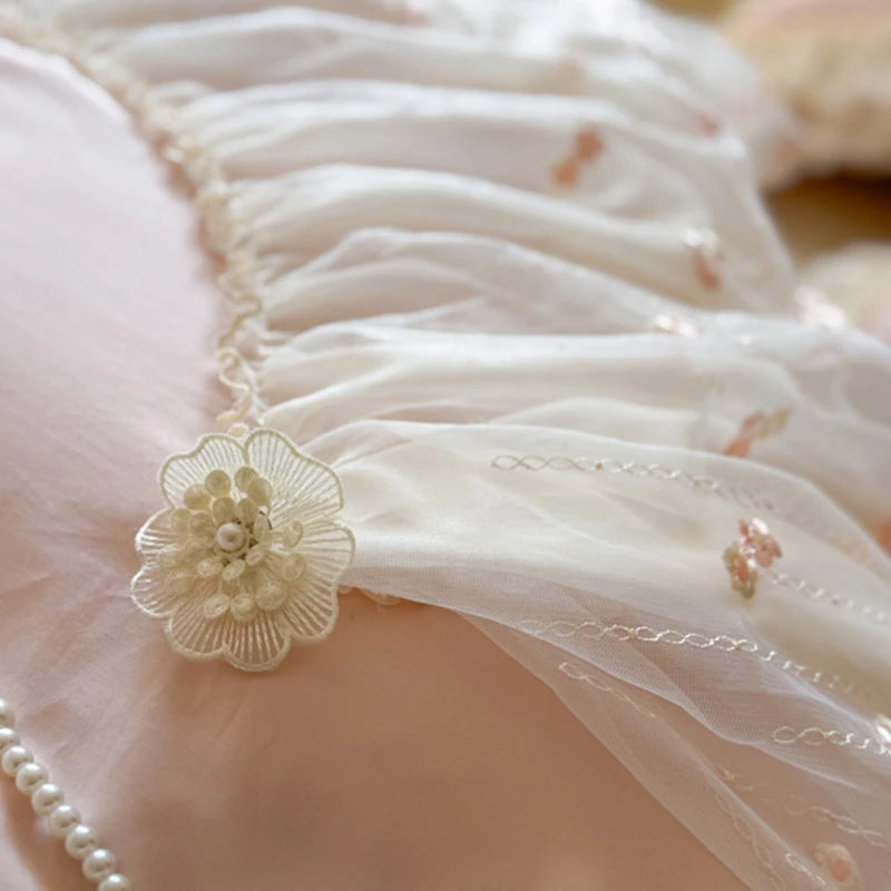Close-up of a bed spread with a floral design and pearls on a soft pink background.