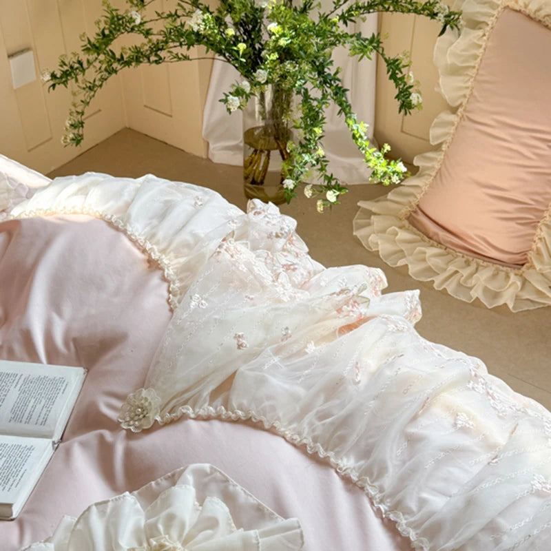 Decorative pillows with lace and floral details on a bed, with a vase of flowers in the background.