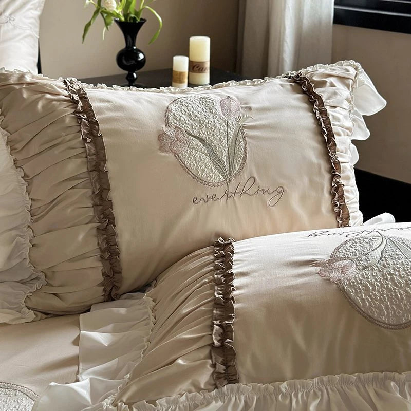 Decorative pillows with ruffled edges and embroidered designs on a bed.