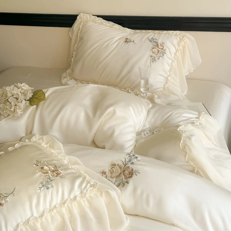 Delicate cream bedding set with floral embroidery on a bed.