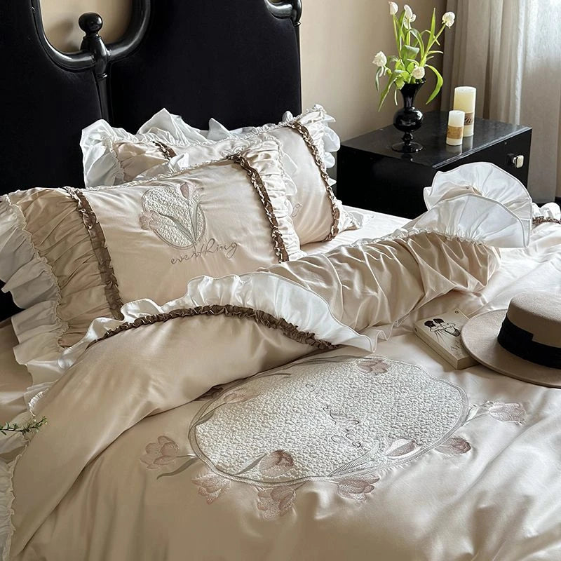 Delicate embroidered bedding set on a bed with a nightstand in the background.
