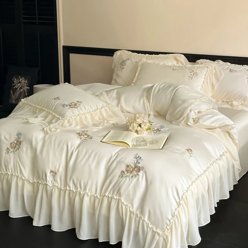 Delicate off white bedding set with floral embroidery on a bed.