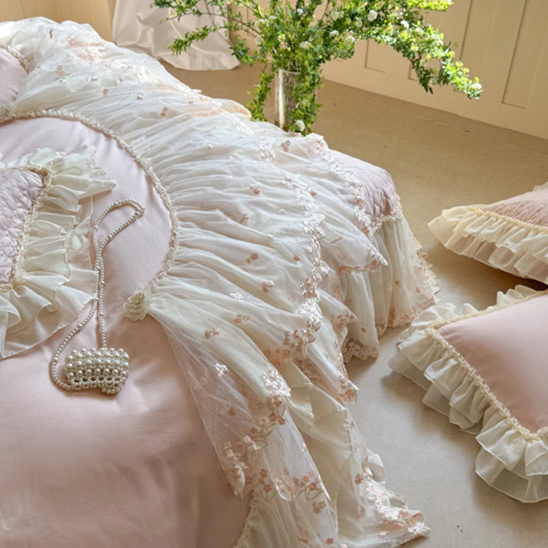 Delicate pink and white bedding with floral embroidery and ruffles on a bed.