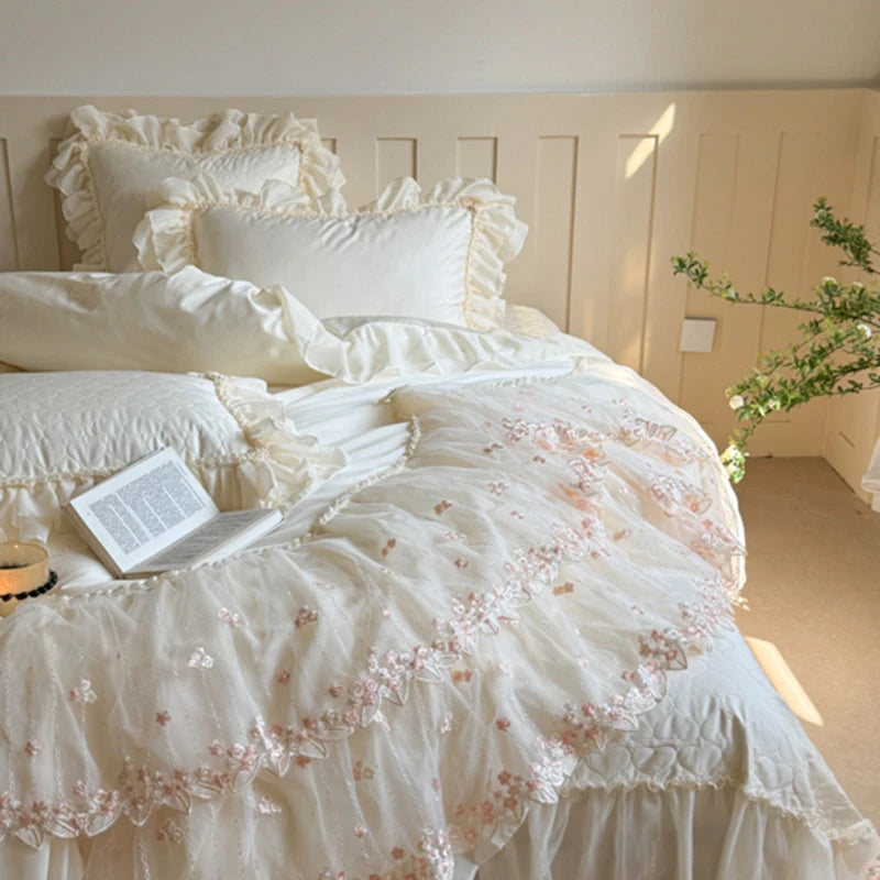Delicate white bedding with floral embroidery on a bed in a softly lit room.