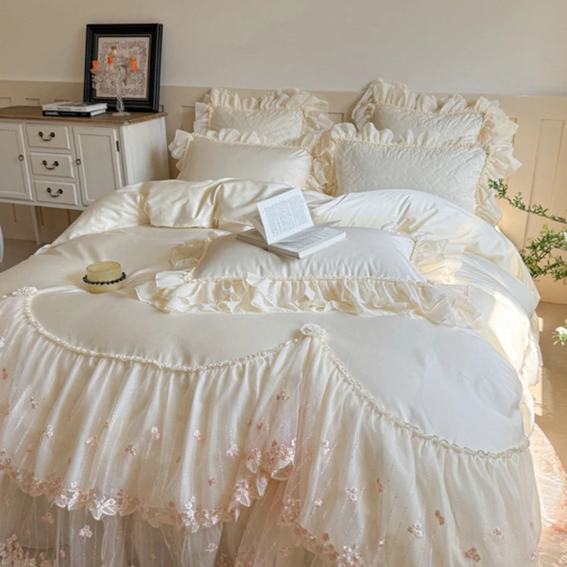 Delicate white ruffled bedding set on a bed with a side table and decor in the background.