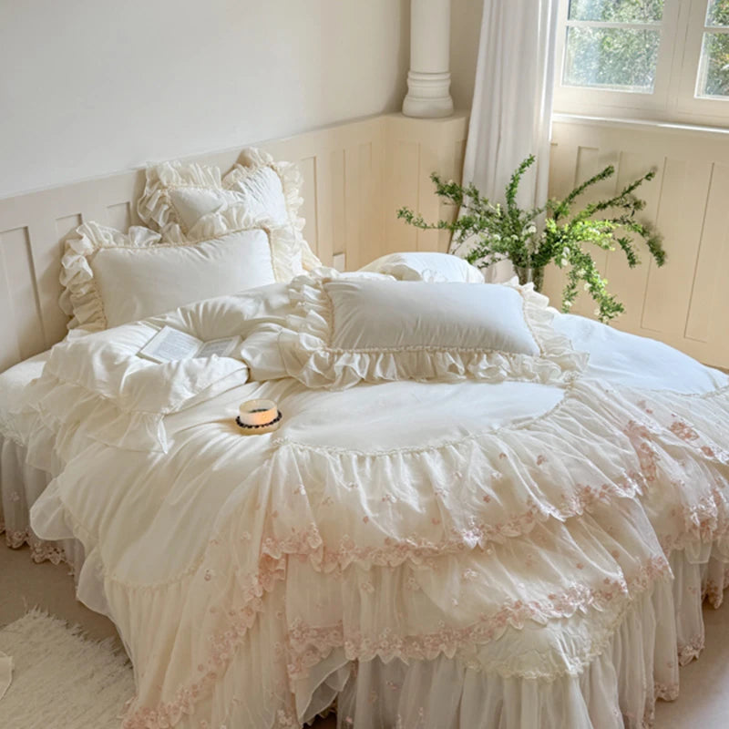 Delicate white ruffled bedding set on a bed with a window in the background.