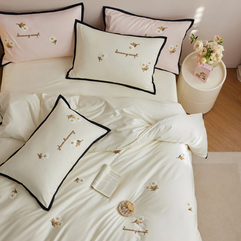 Embroidered bedding set with decorative pillows on a bed in a bedroom setting.