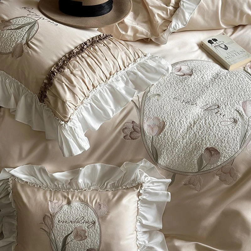 Embroidered beige bedding set with floral patterns on a bed.