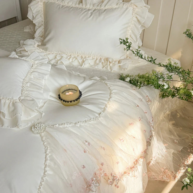 Floral bedding set with ruffles on a bed, featuring a candle and greenery.