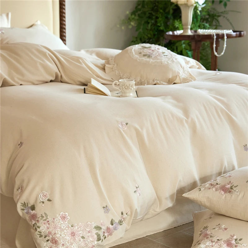 Floral embroidered bedding set on a bed with a cup and book in a bedroom setting.