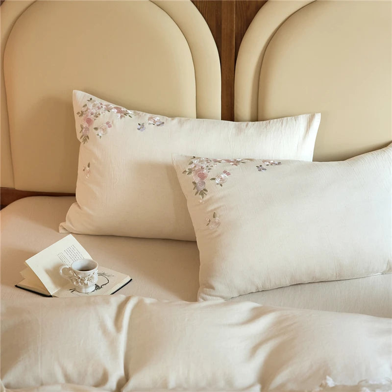 Floral embroidered pillows on a bed with a book and cup in the foreground.