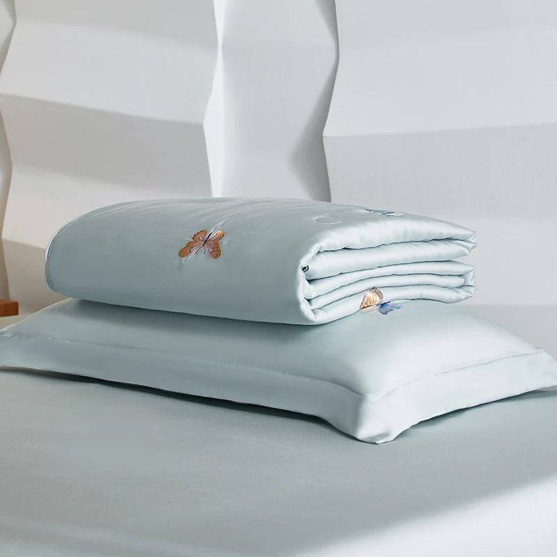 Folded light blue bed sheets with embroidered designs on a white background