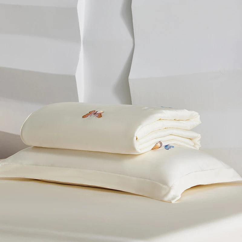 Folded white bed sheets with embroidered designs on a white background