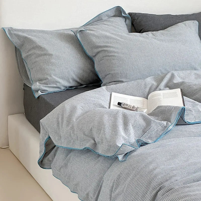 Gray and blue striped bedding set on a bed with a gray pillow and gray blanket.