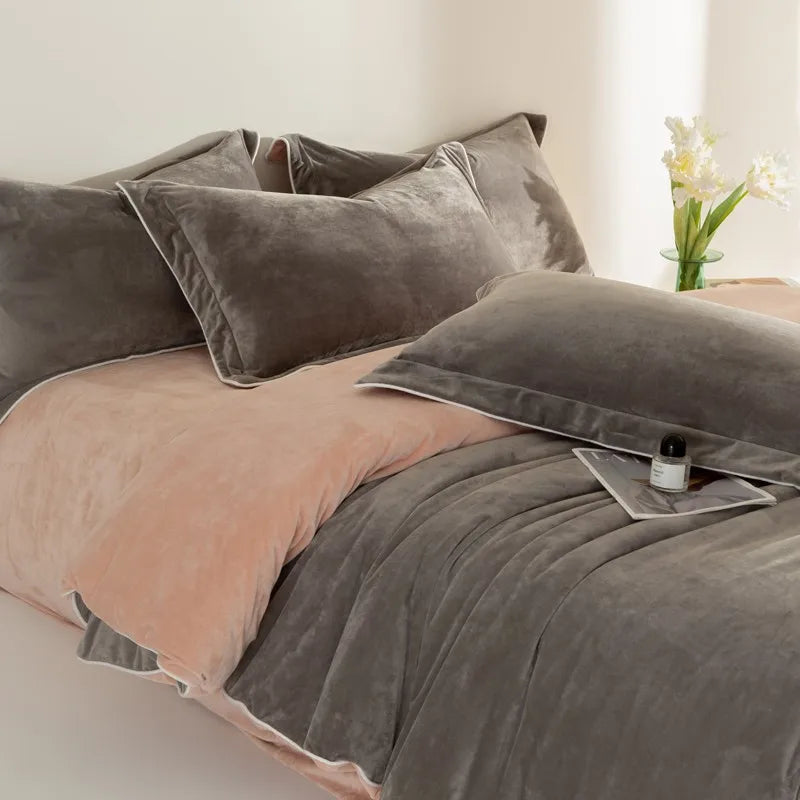 Gray and peach bedding set on a bed with a small table and flowers in the background.