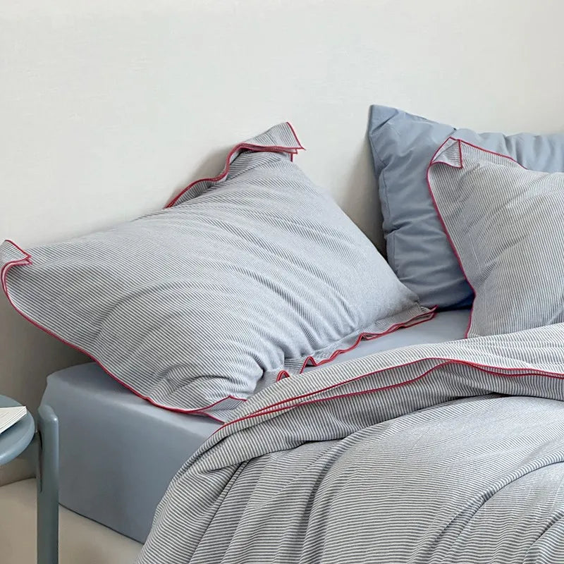 Gray bedding with red trim on a bed against a white wall