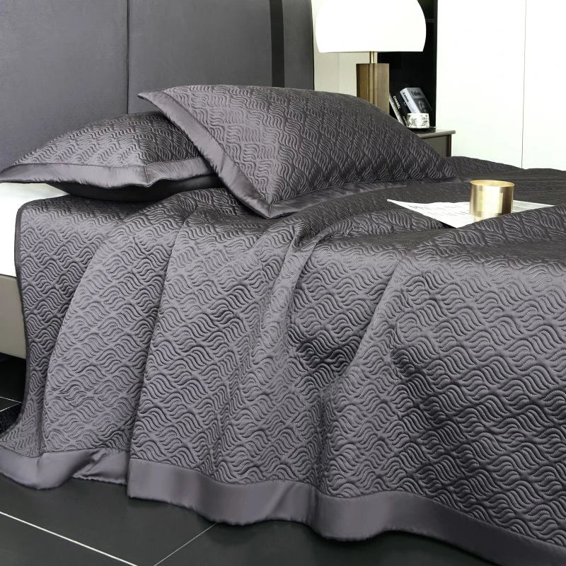 Gray quilt with geometric pattern on a bed in a bedroom setting.