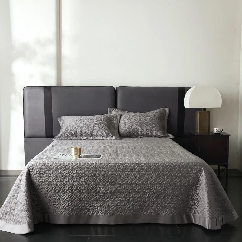 Gray quilted bedspread on a bed with matching pillows in a minimalistic bedroom.