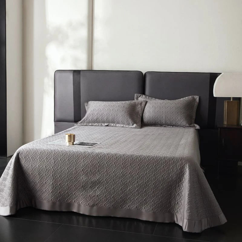 Gray quilted bedspread on a bed with pillows in a bedroom setting.