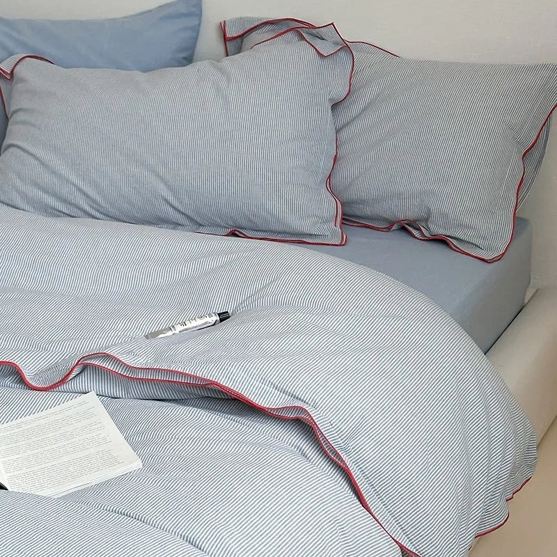 Gray striped bedding with red trim on a bed