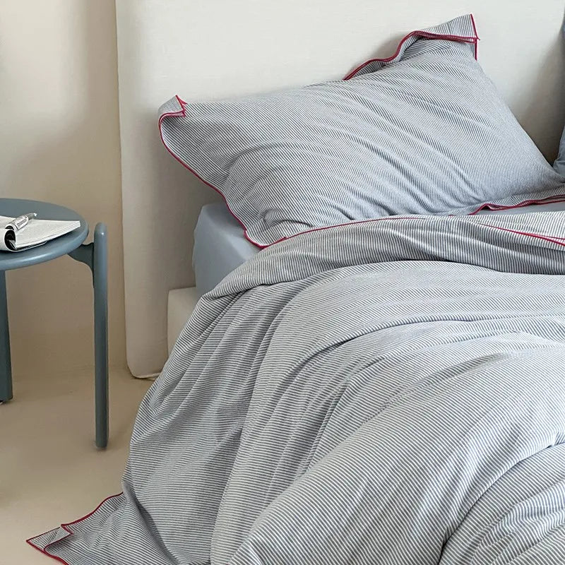 Gray striped bedding with red trim on a bed in a bedroom setting.