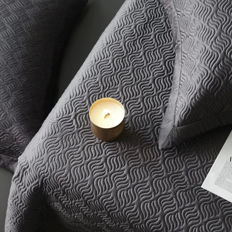 Gray textured bed spread with a lit candle on a dark surface