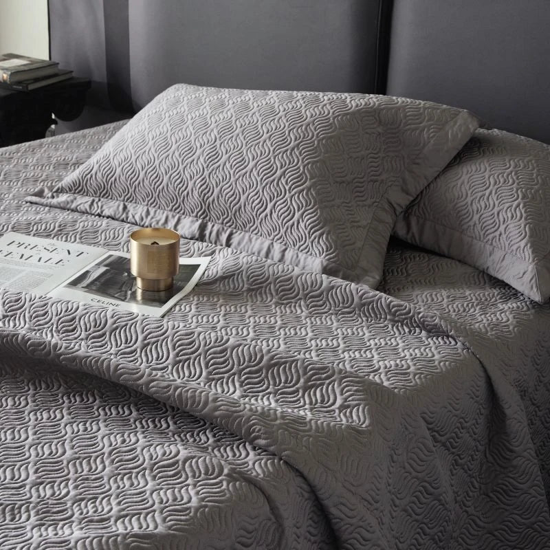 Gray textured blanket draped over a bed with a candle and newspaper on top.