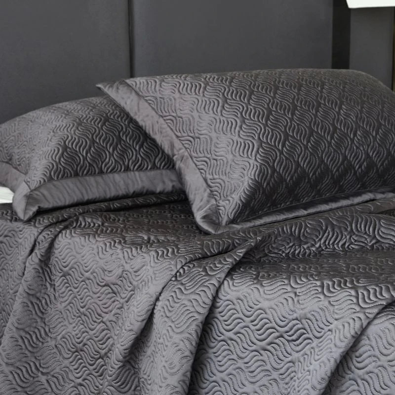 Gray textured quilt and pillow set on a bed with a dark headboard.