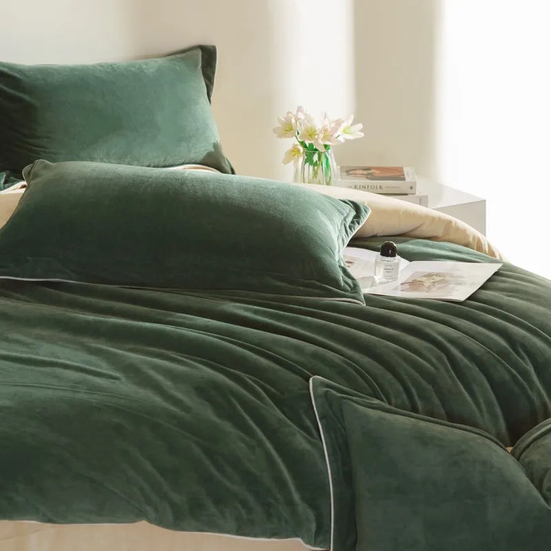 Green velvet bedding set on a bed with a side table and flowers in the background.