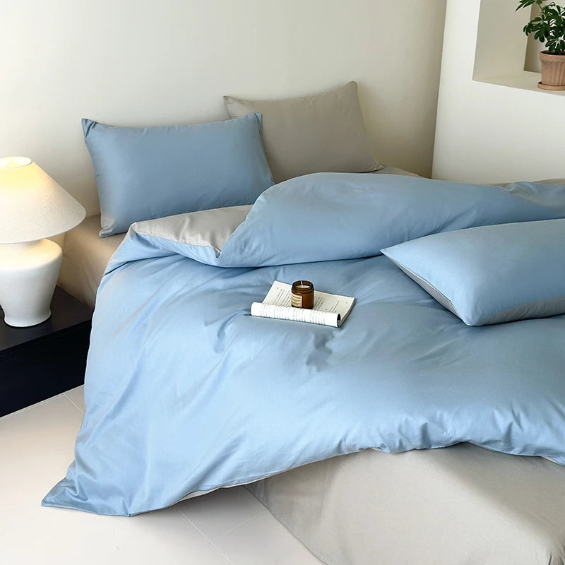Light blue bedding set on a bed with a nightstand and lamp in a bedroom setting.