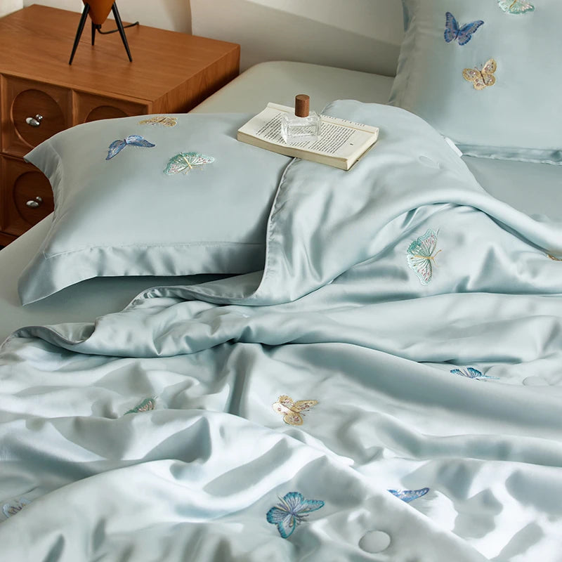 Light blue bedding set with embroidered butterflies on a bed in a bedroom.