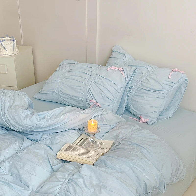 Light blue bedding set with pink ribbons on a bed with a candle and book.